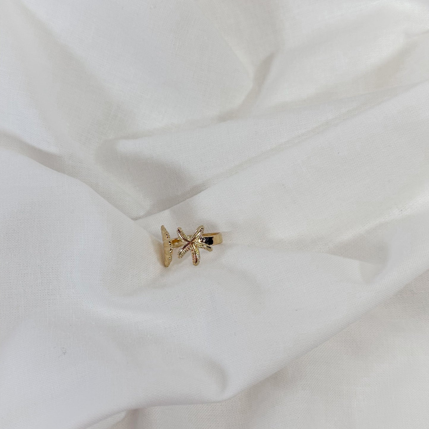 Gold starfish-shaped ring on a white fabric background
