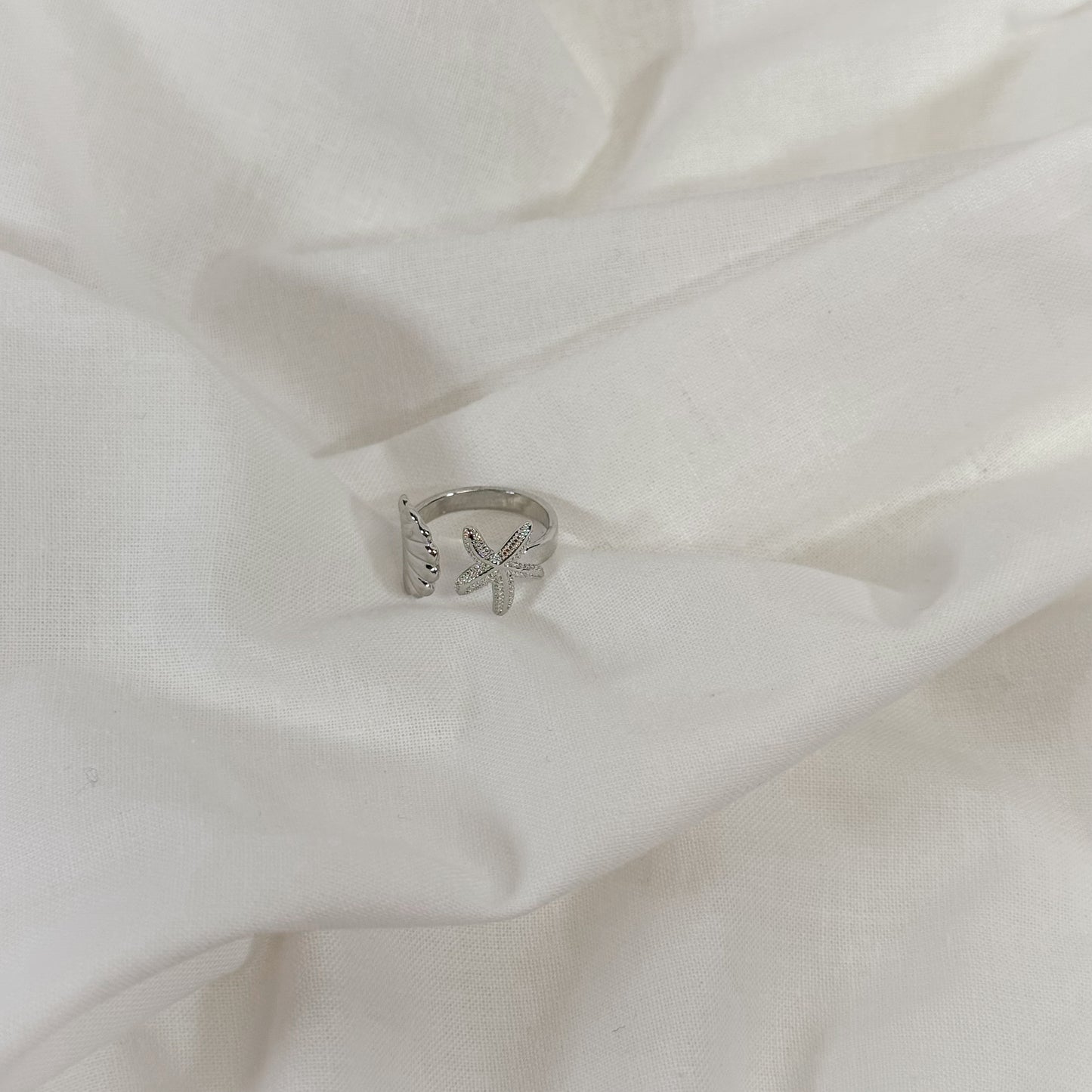 Silver ring with a shell design on a white fabric background