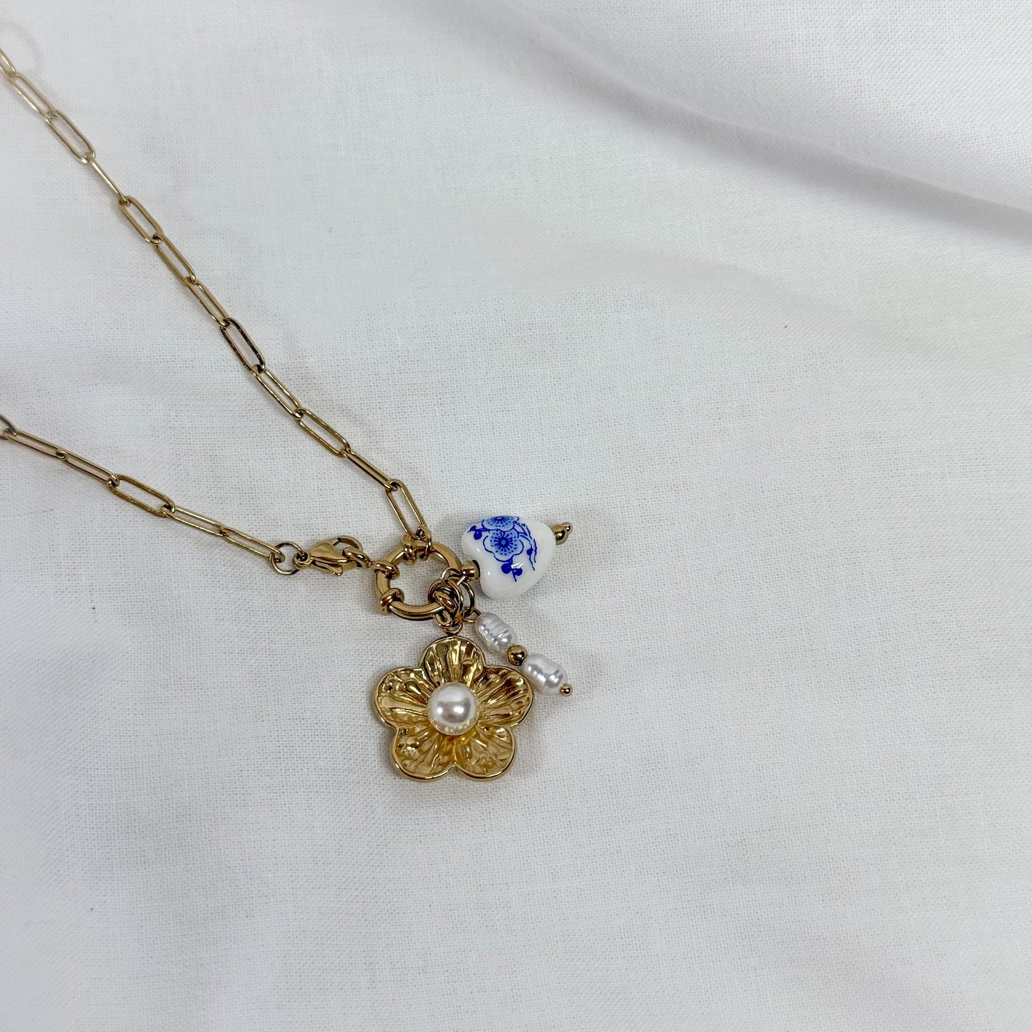 Necklace with gold flower charm, pearl, and blue heart pendant on a white background