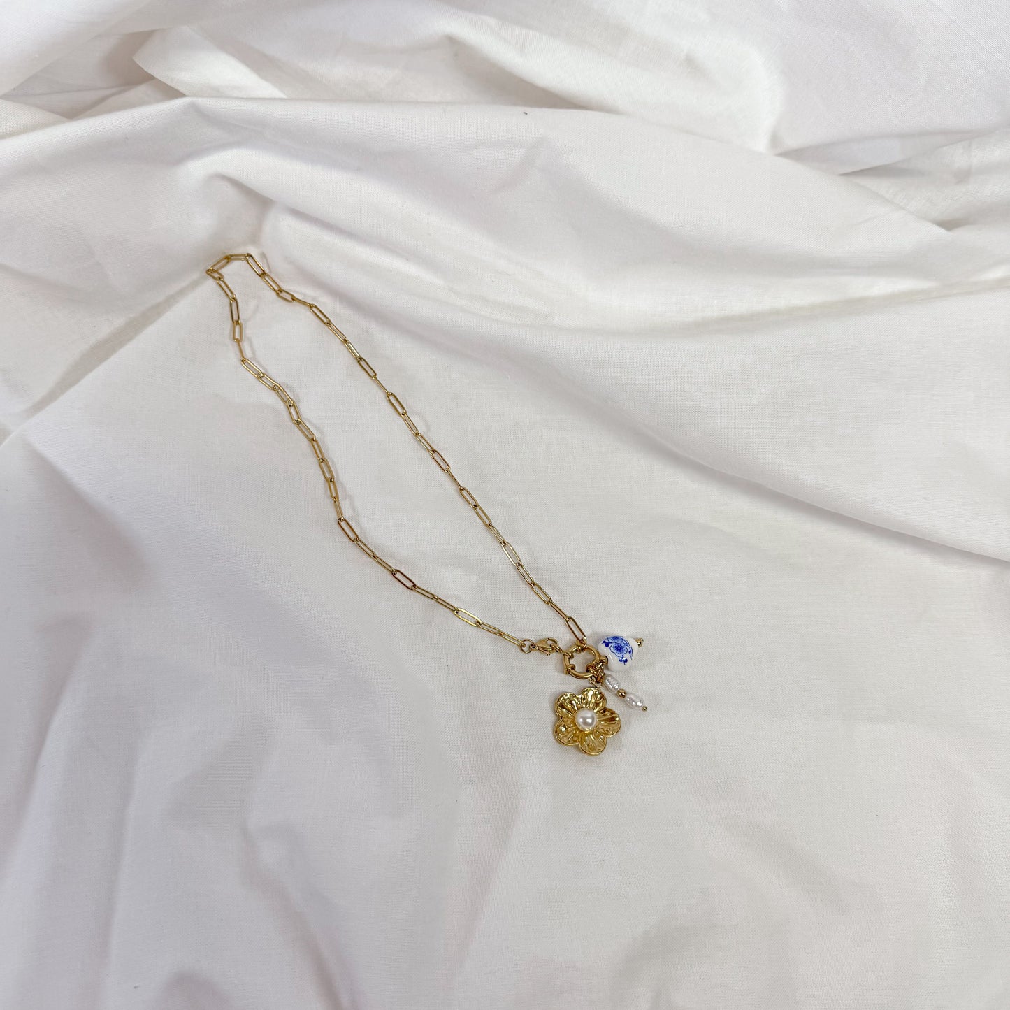 Gold necklace with a porcelain flower pendant on a white fabric background