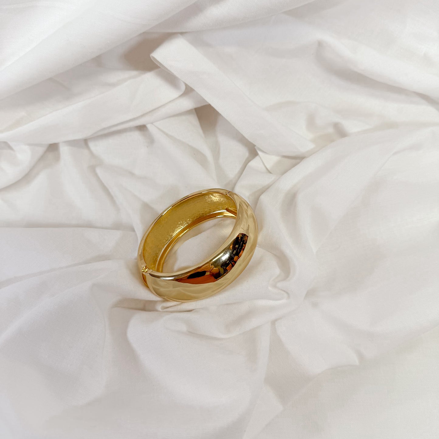 Thick gold bangle bracelet on a white fabric background