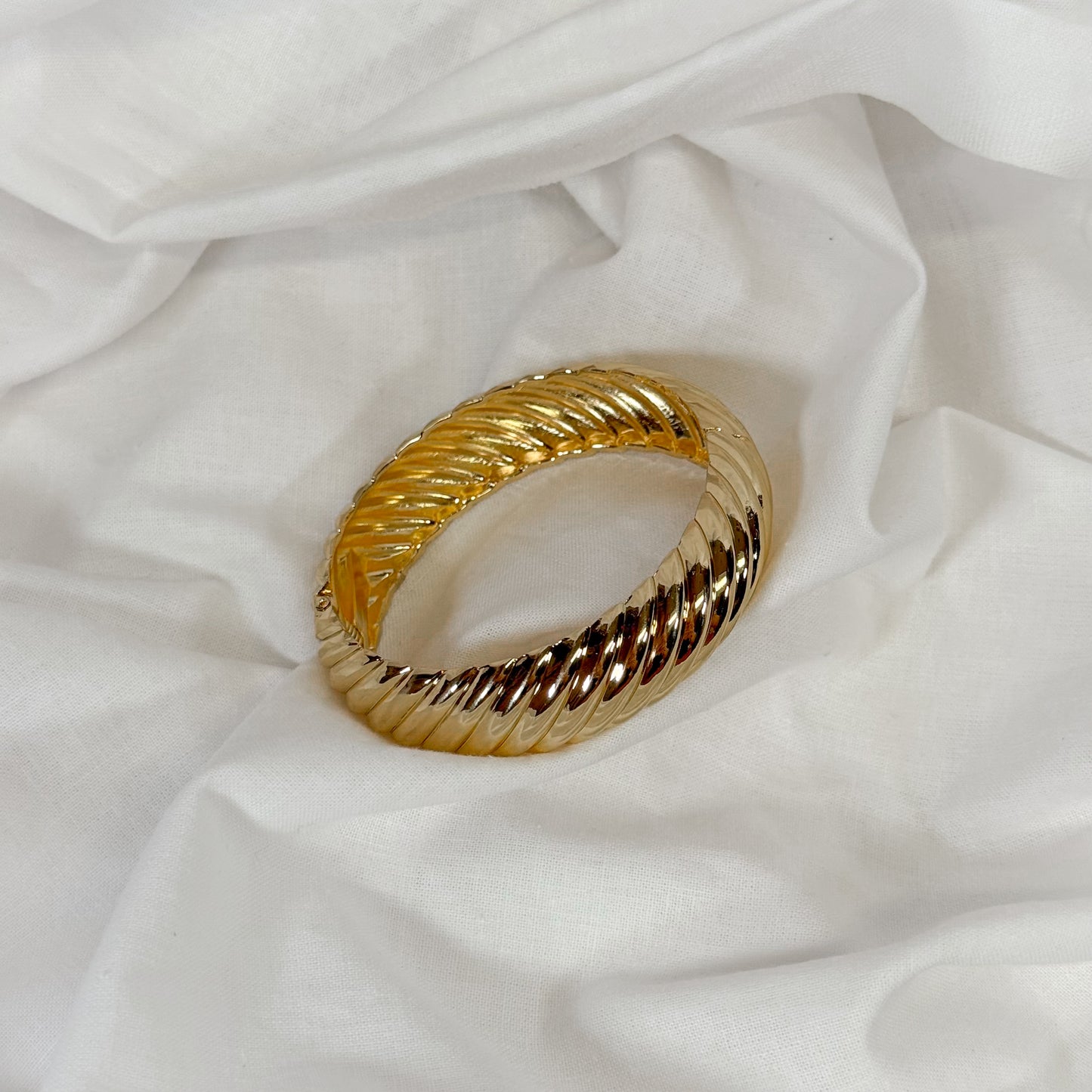 Patterned chunky gold bangle on a white fabric background
