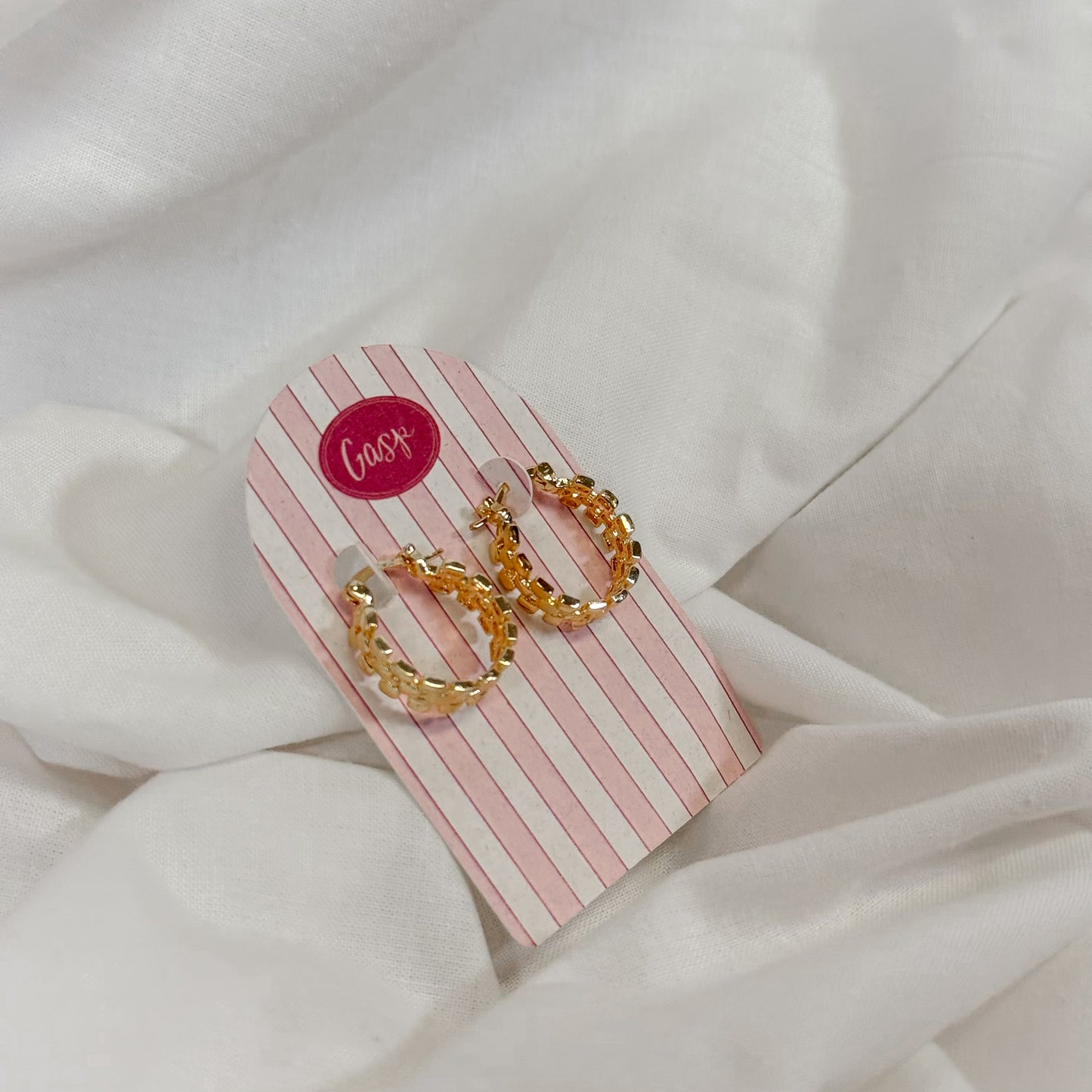 Chain link style gold hoop earrings on a striped card with 'Gasp' branding, placed on a white fabric background.