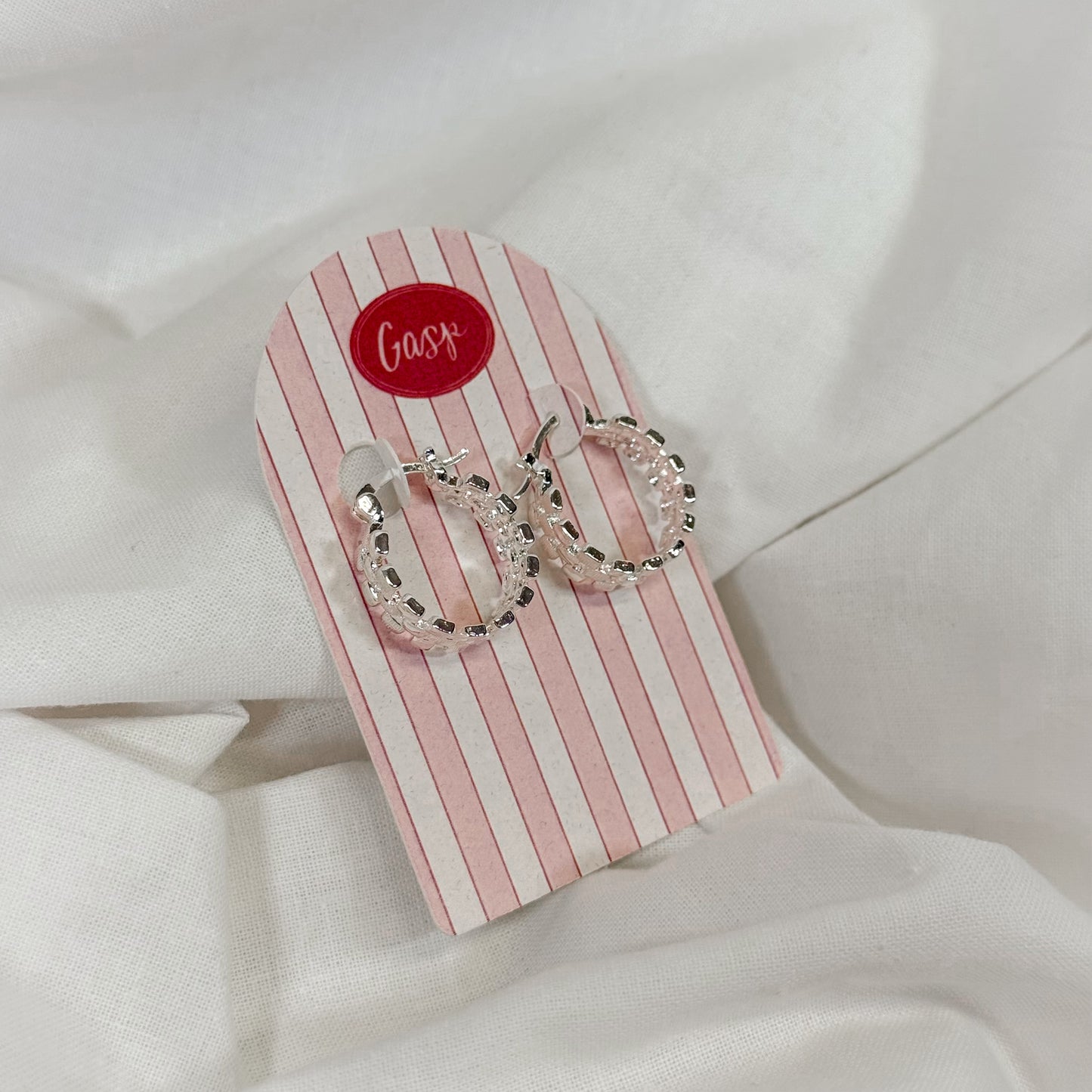 Silver hoop earrings on a striped card with 'Gasp' brand name, on a white fabric background