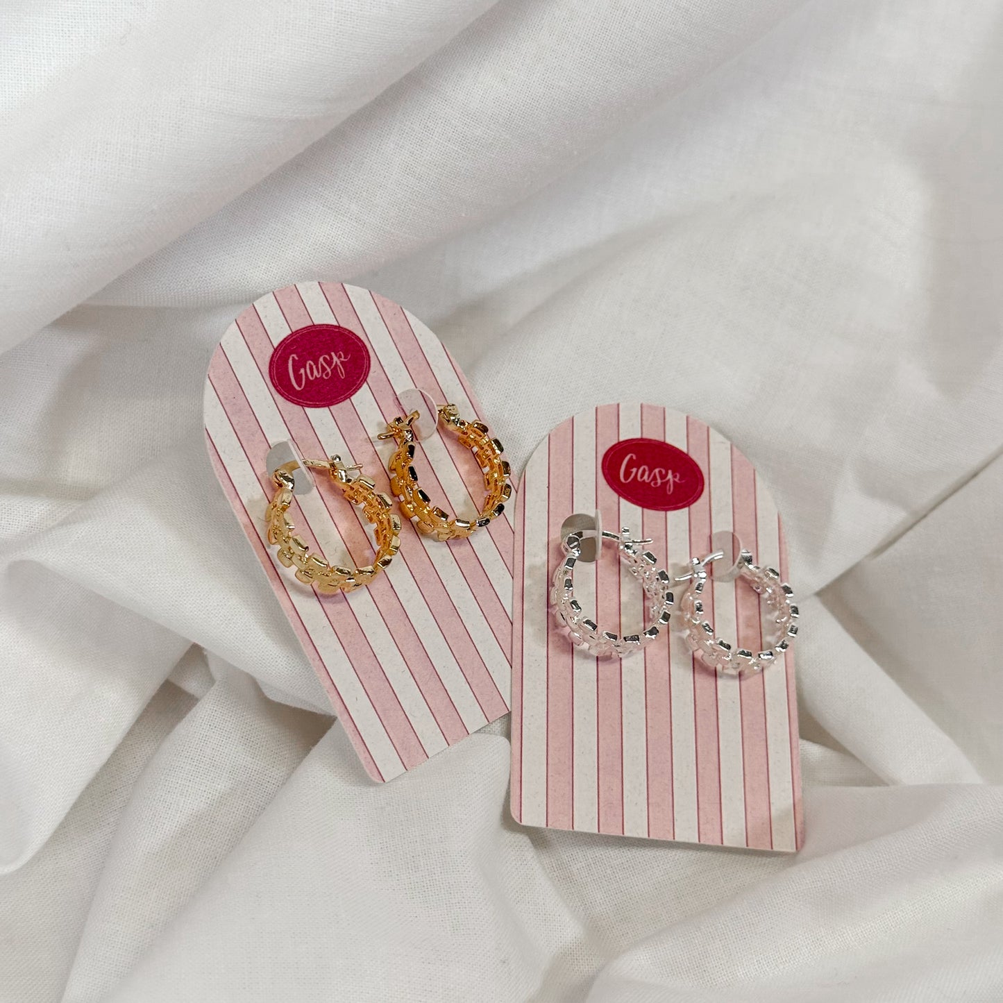 Two pairs of earrings on pink and white striped cards with 'Gasp' branding on a white fabric background.