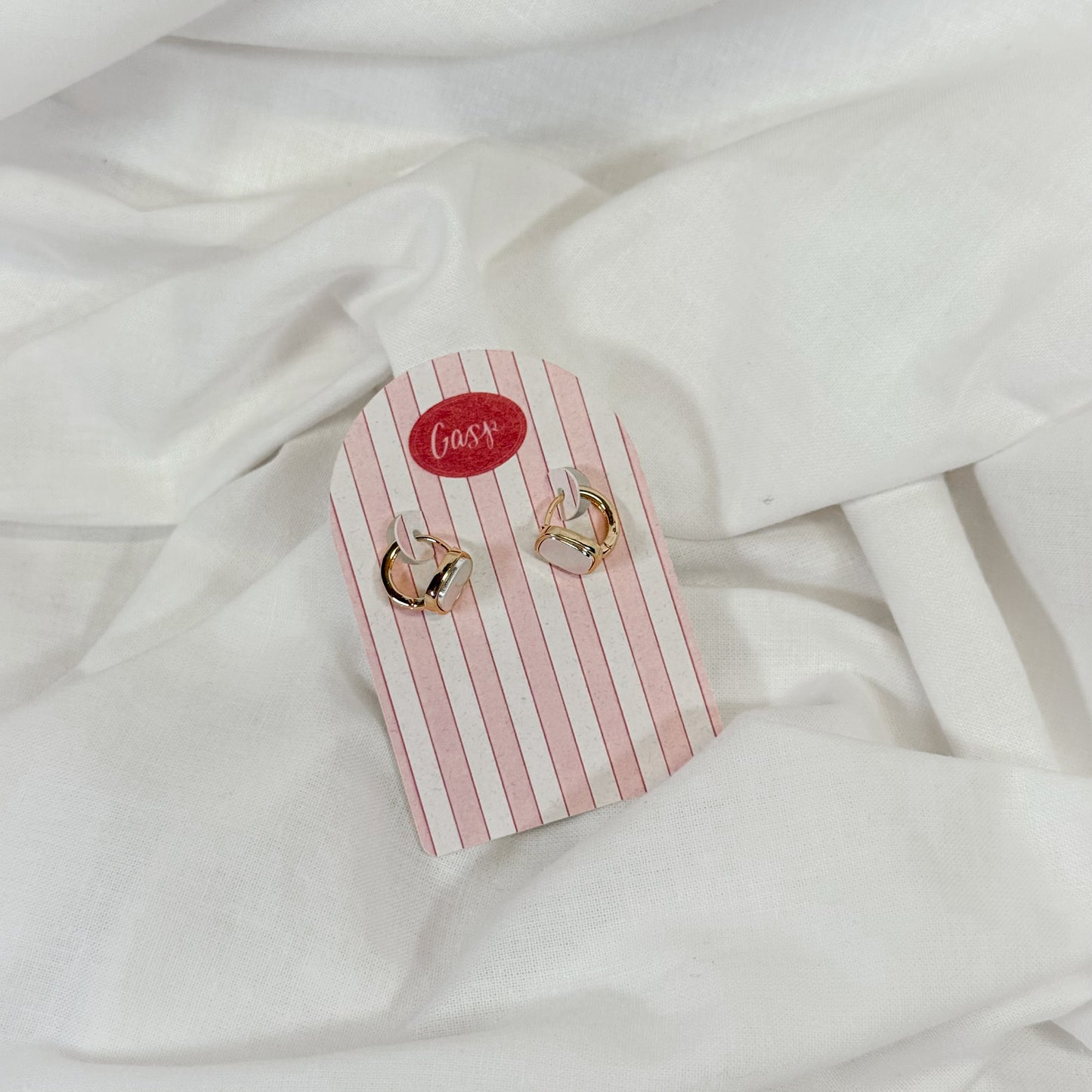 Pair of gold and pearl hoop earrings on a pink and white striped card with 'Gasp' branding, placed on a white fabric background.