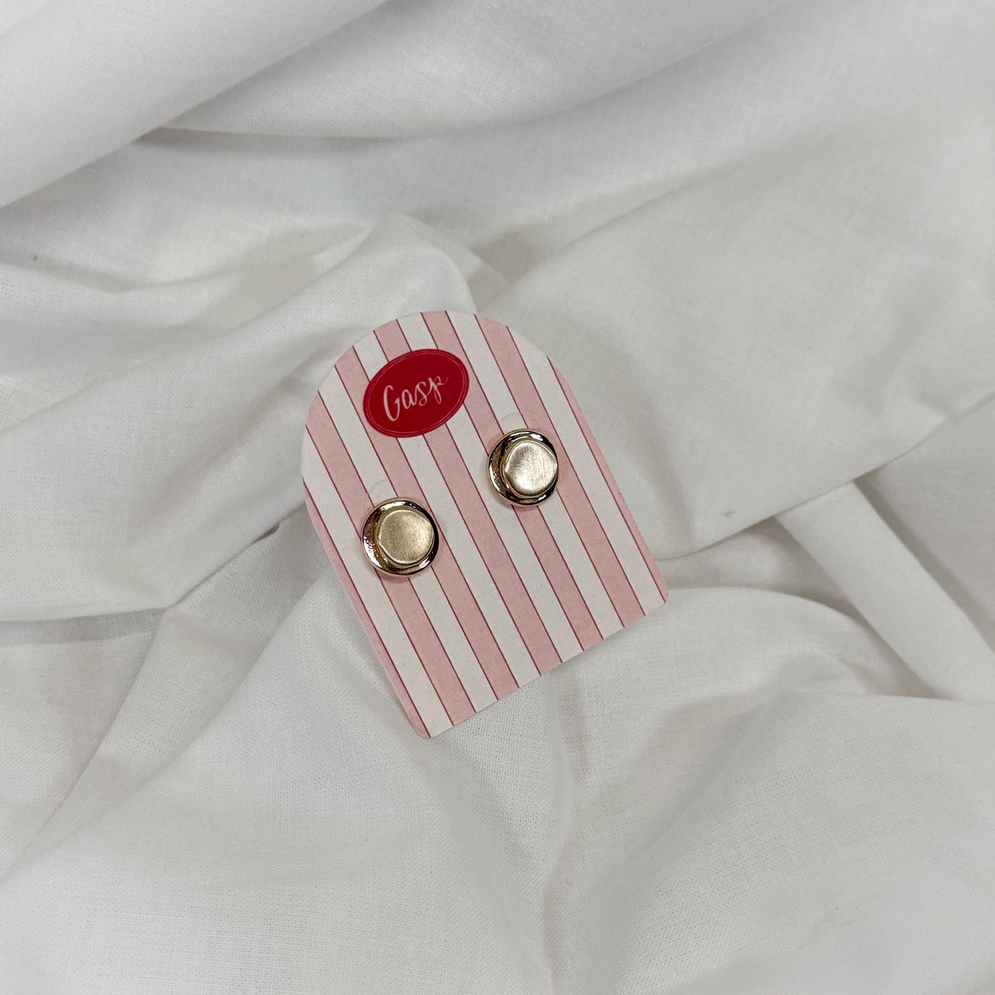 Round gold earrings on a pink and white striped card with 'Gasp' branding, placed on a white fabric background.