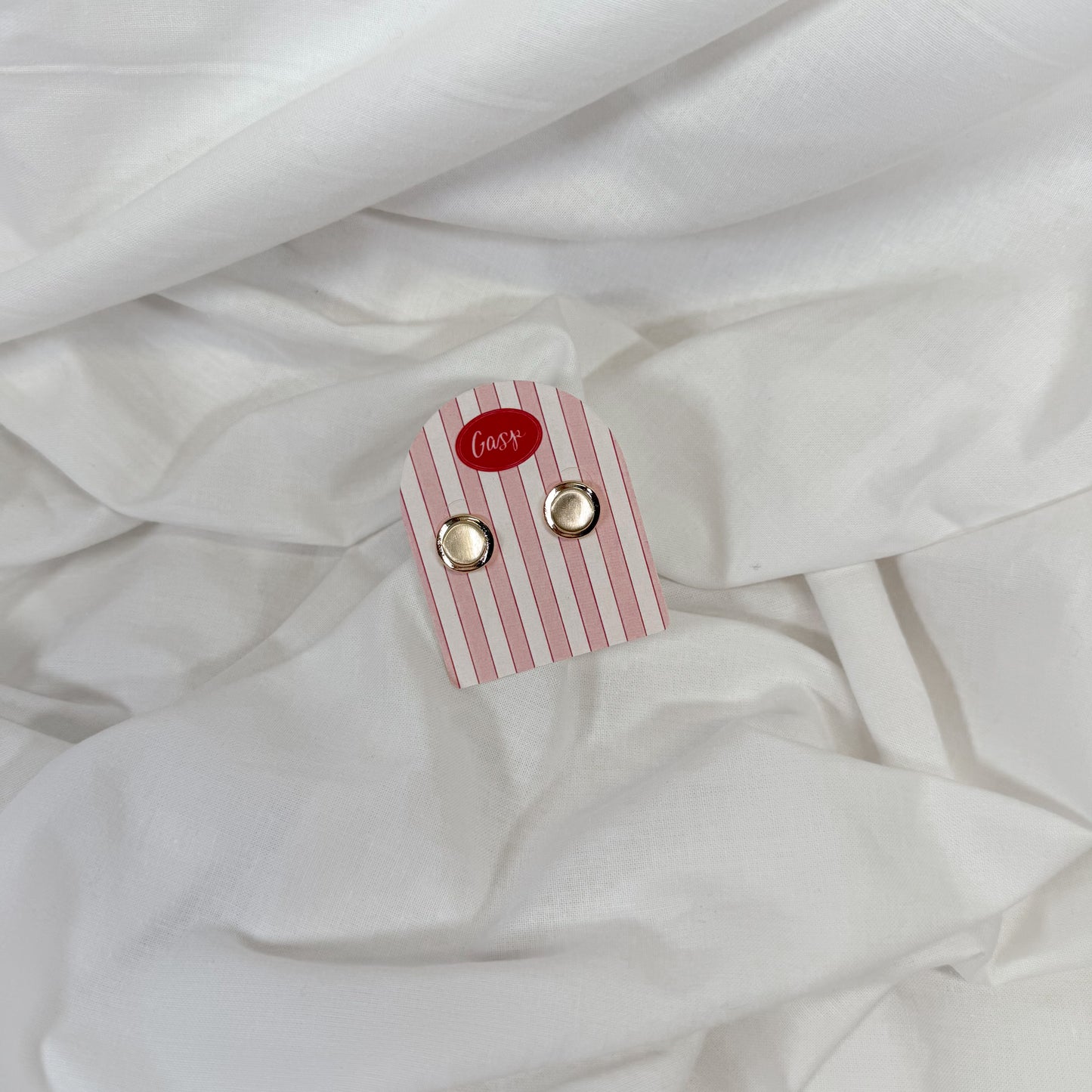 Chunky golf earrings on a pink and white striped card with 'Gasp' brand name, placed on white fabric.