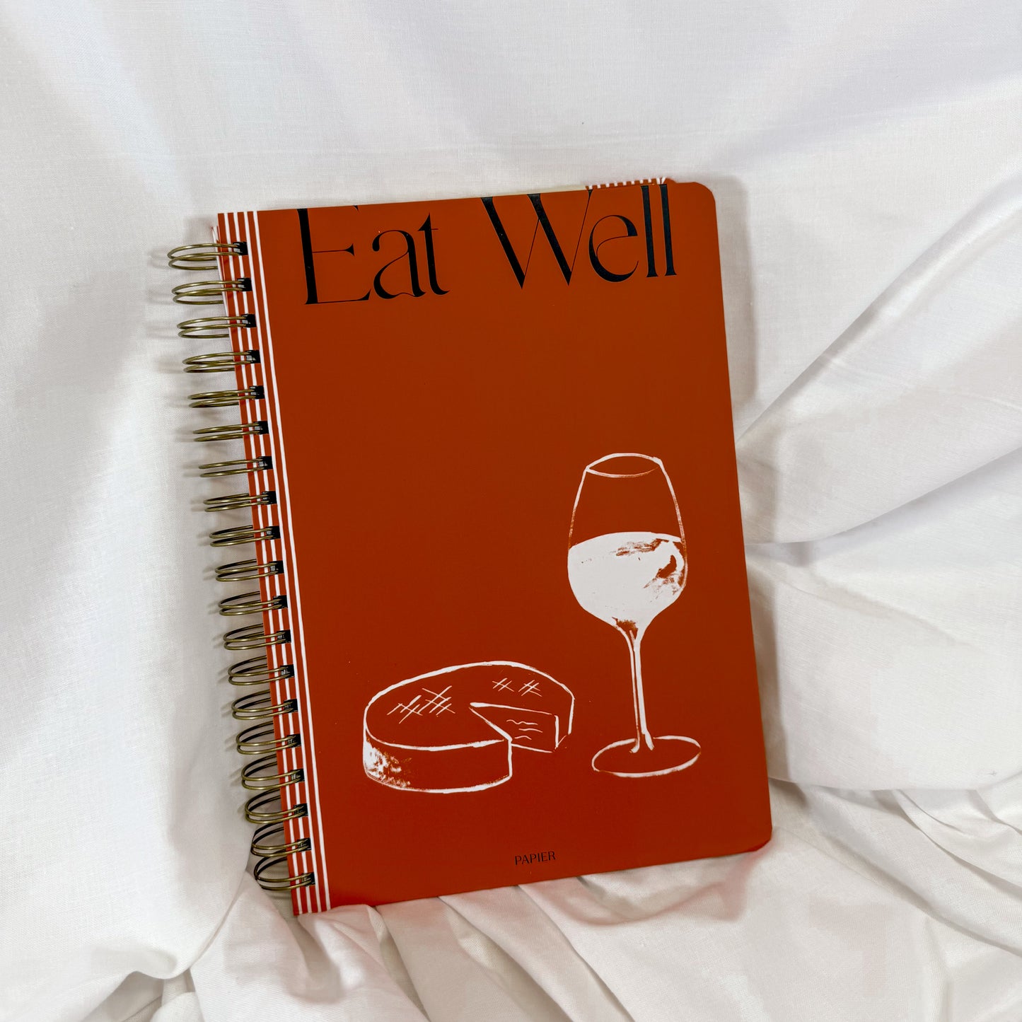 Spiral bound Eat Well recipe journal with wine and cheese illustration on rust-colored cover