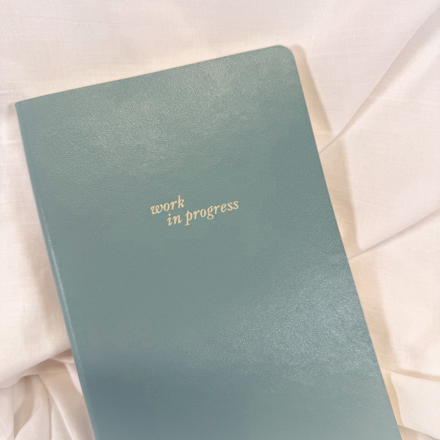 Blue notebook with 'work in progress' text on a light fabric background