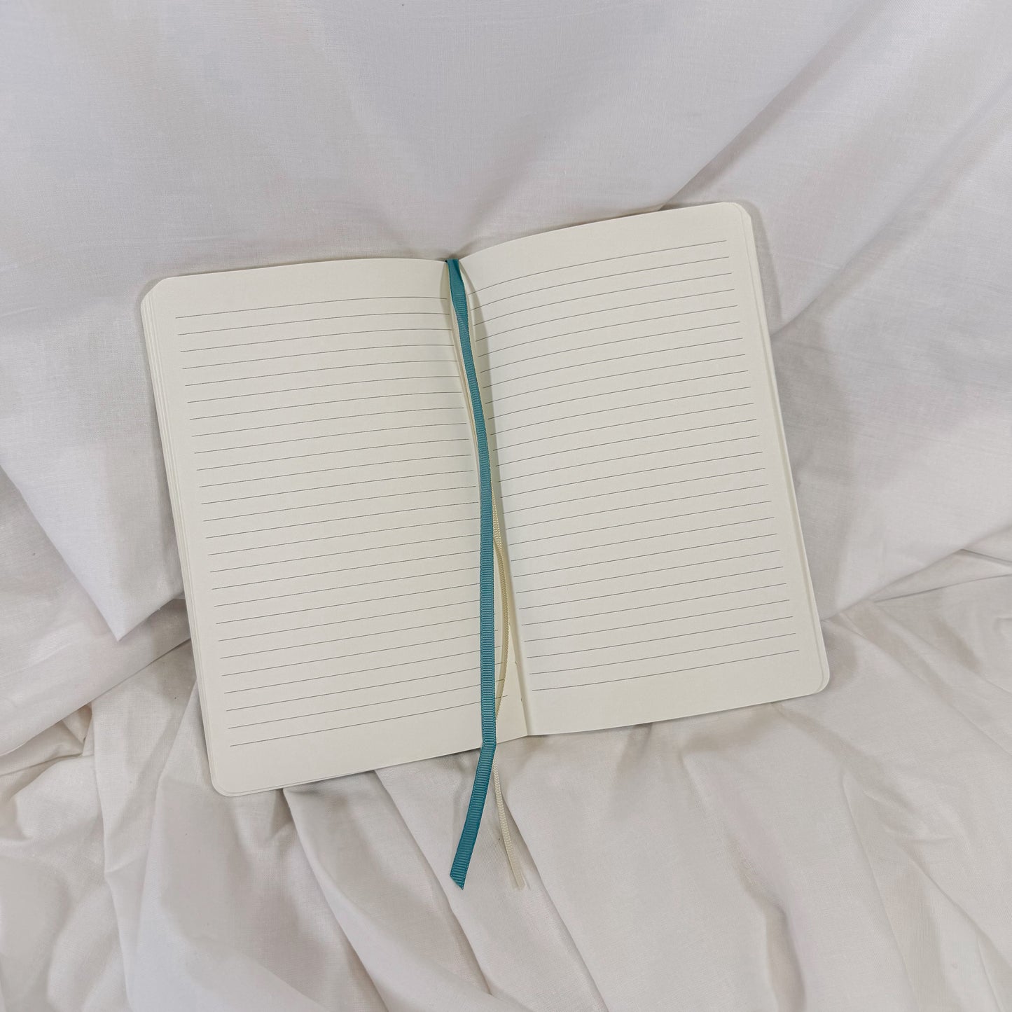 Open notebook with a blue ribbon bookmark on a white fabric background
