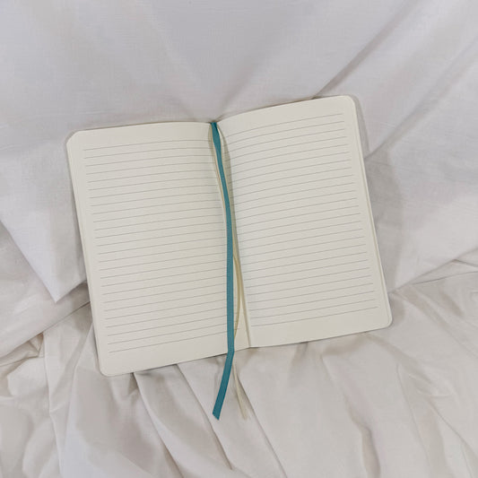 Open notebook with a blue ribbon bookmark on a white fabric background