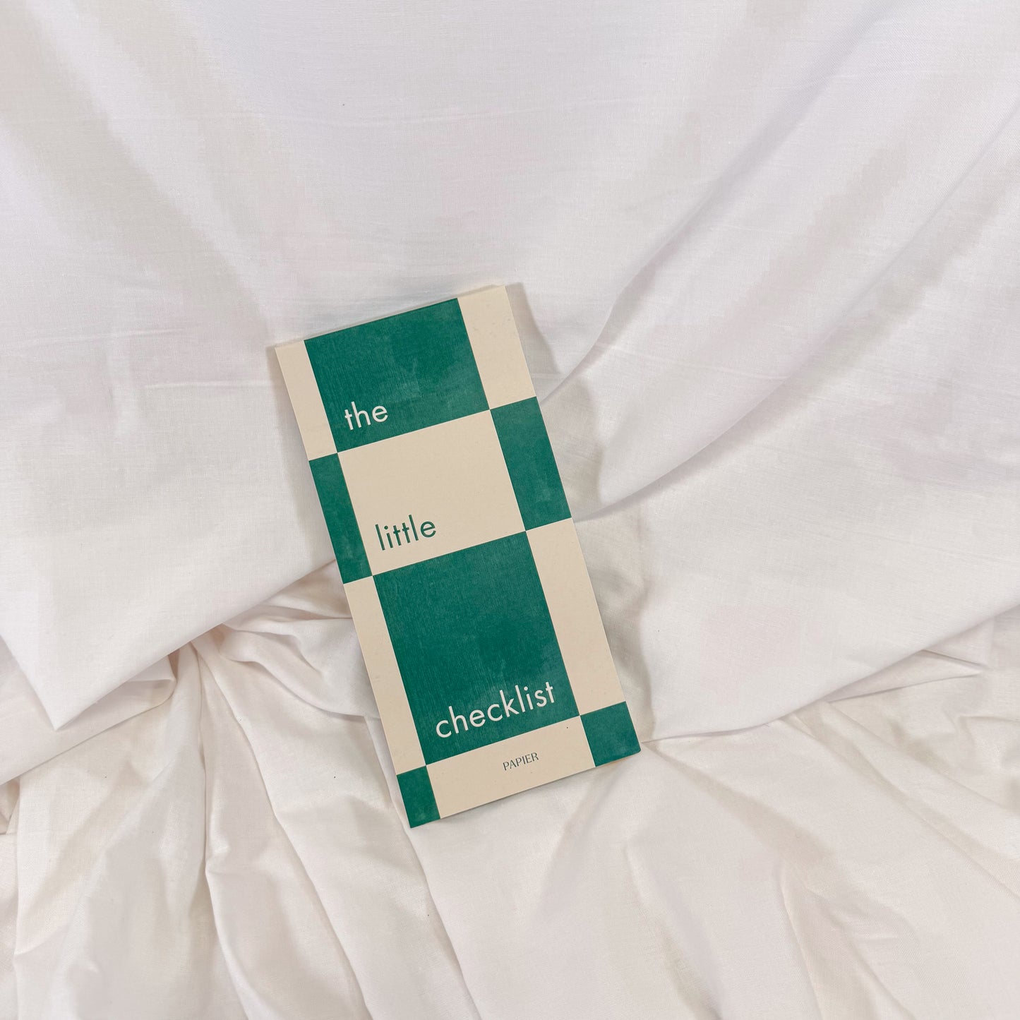 Checklist to do list notepad with green and beige checkered design on a white fabric background