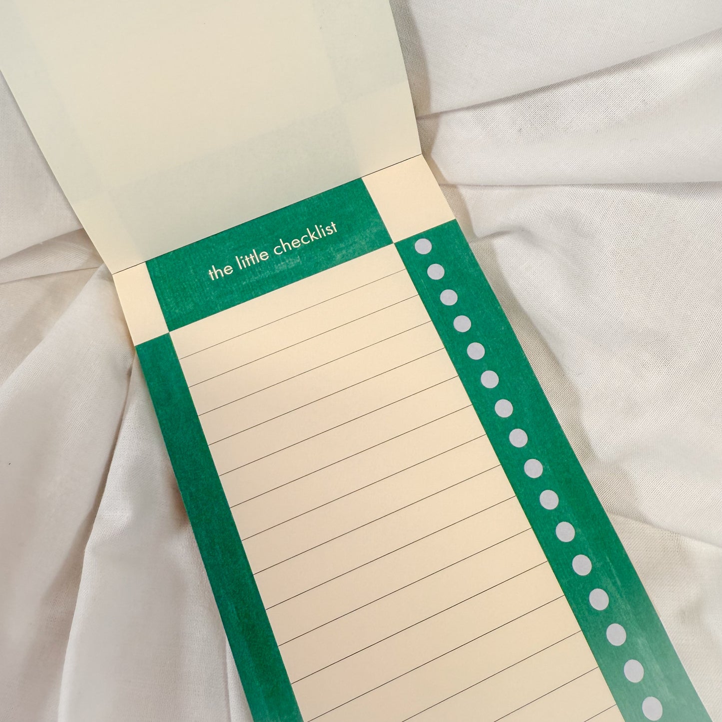 Aesthetic green checkered notepad for daily tasks, open on a white fabric background