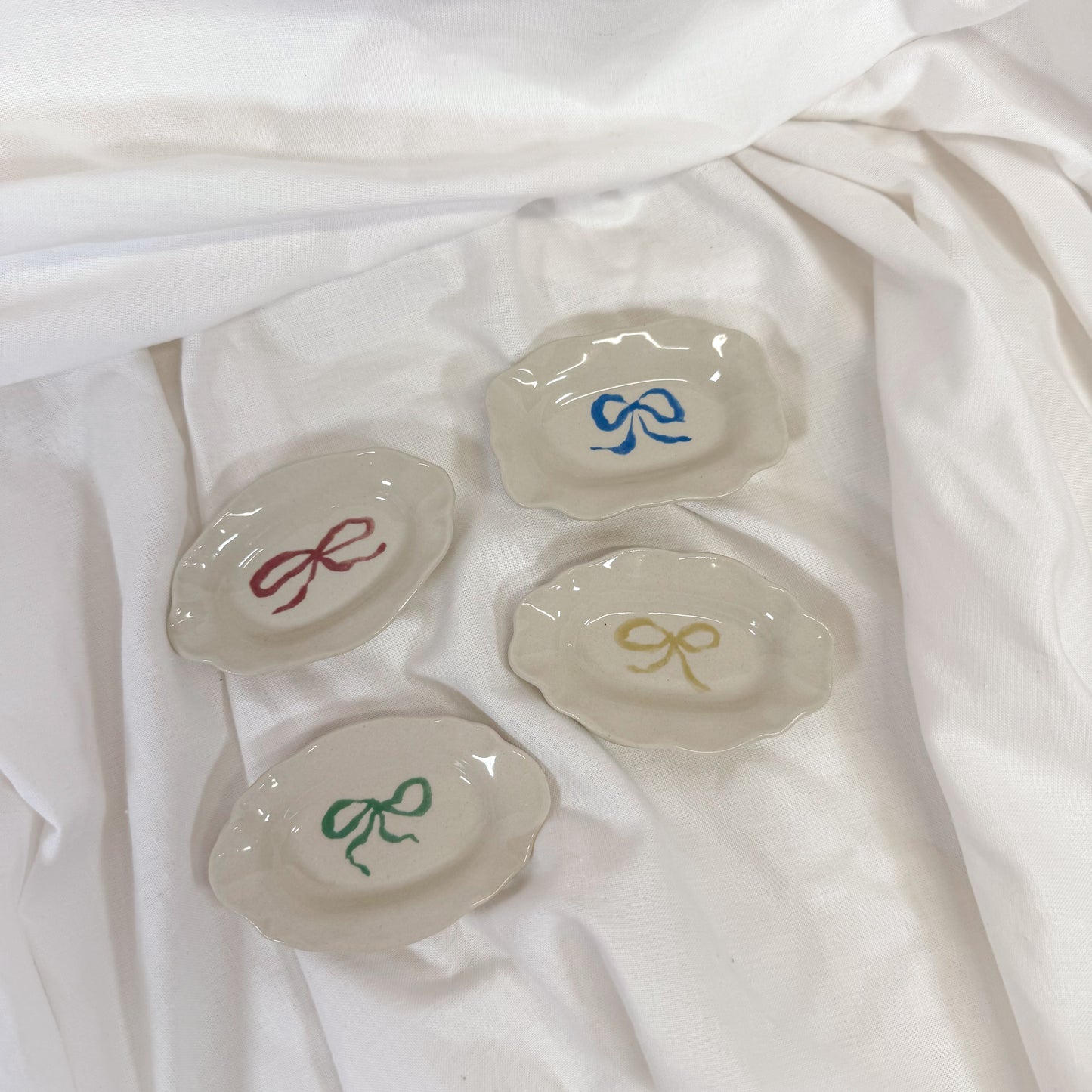 Set of four small ceramic dishes with colorful bow designs on a white fabric background