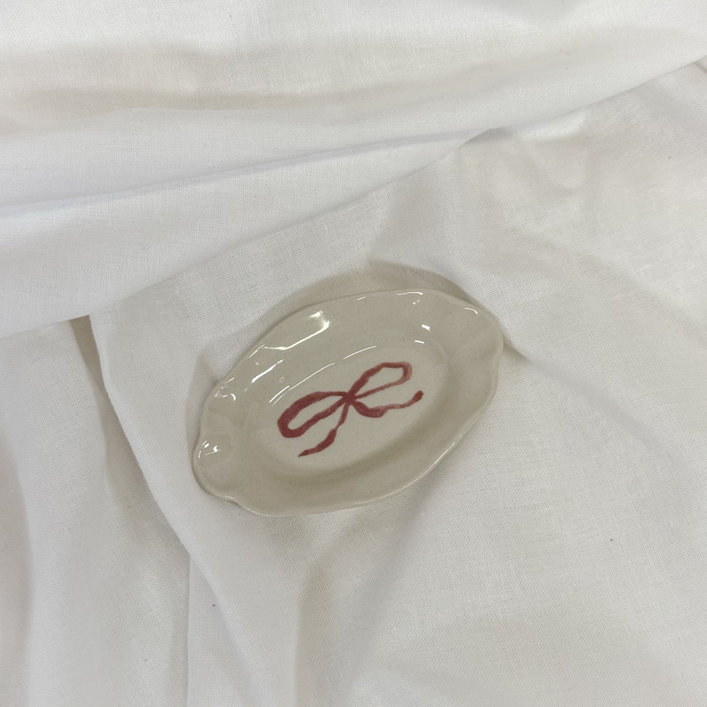 Small oval dish with a red bow design on a white fabric background