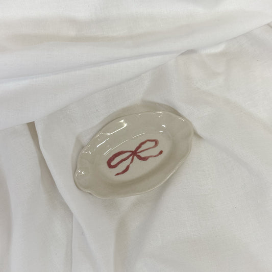 Small oval dish with a red bow design on a white fabric background