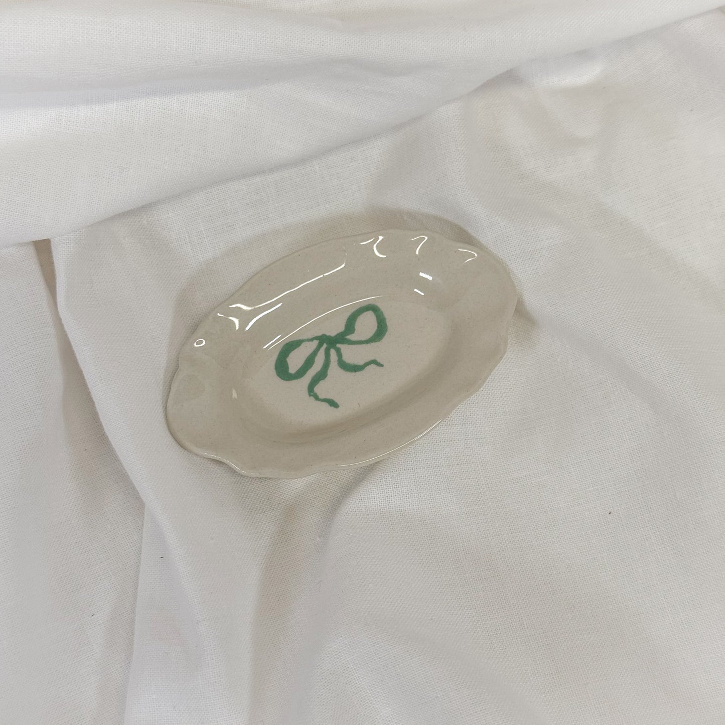 Small ceramic dish with a green design on a white fabric background