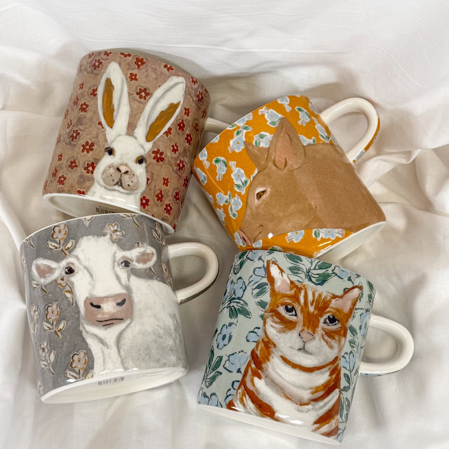 Four mugs with animal designs and floral motifs on a white surface