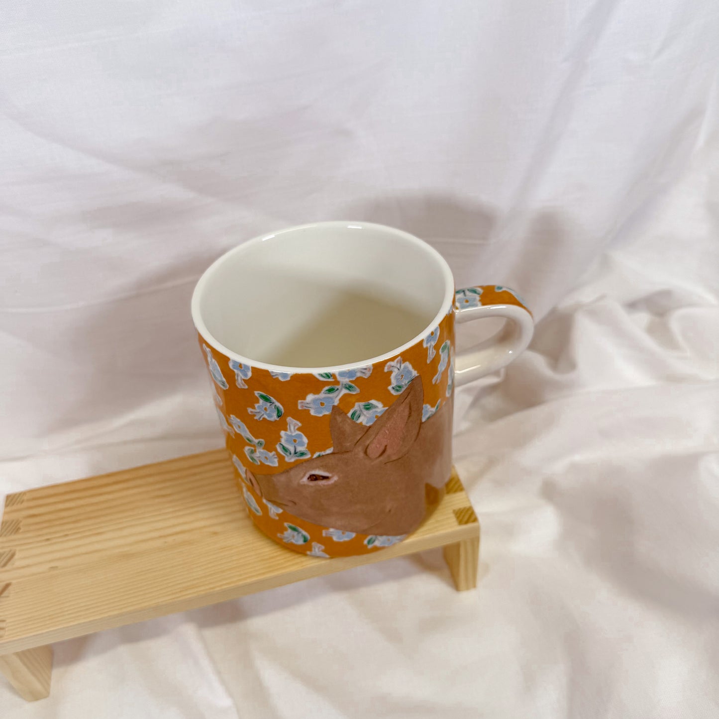 Orange mug with animal pattern on a wooden coaster against a white background