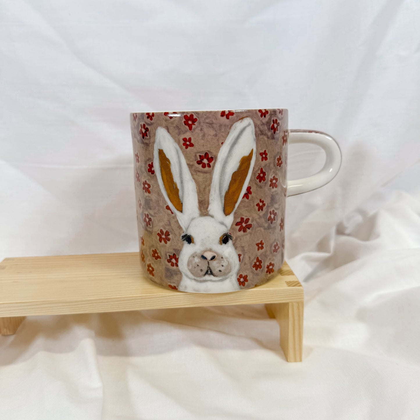 Floral mug with rabbit design on a wooden stand against a white background