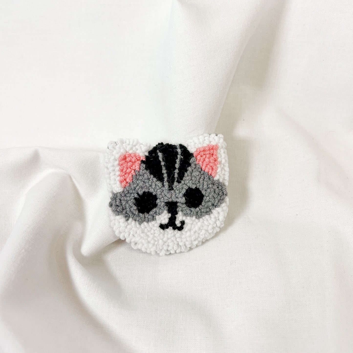 Cat-shaped tufted car coaster on a white fabric background