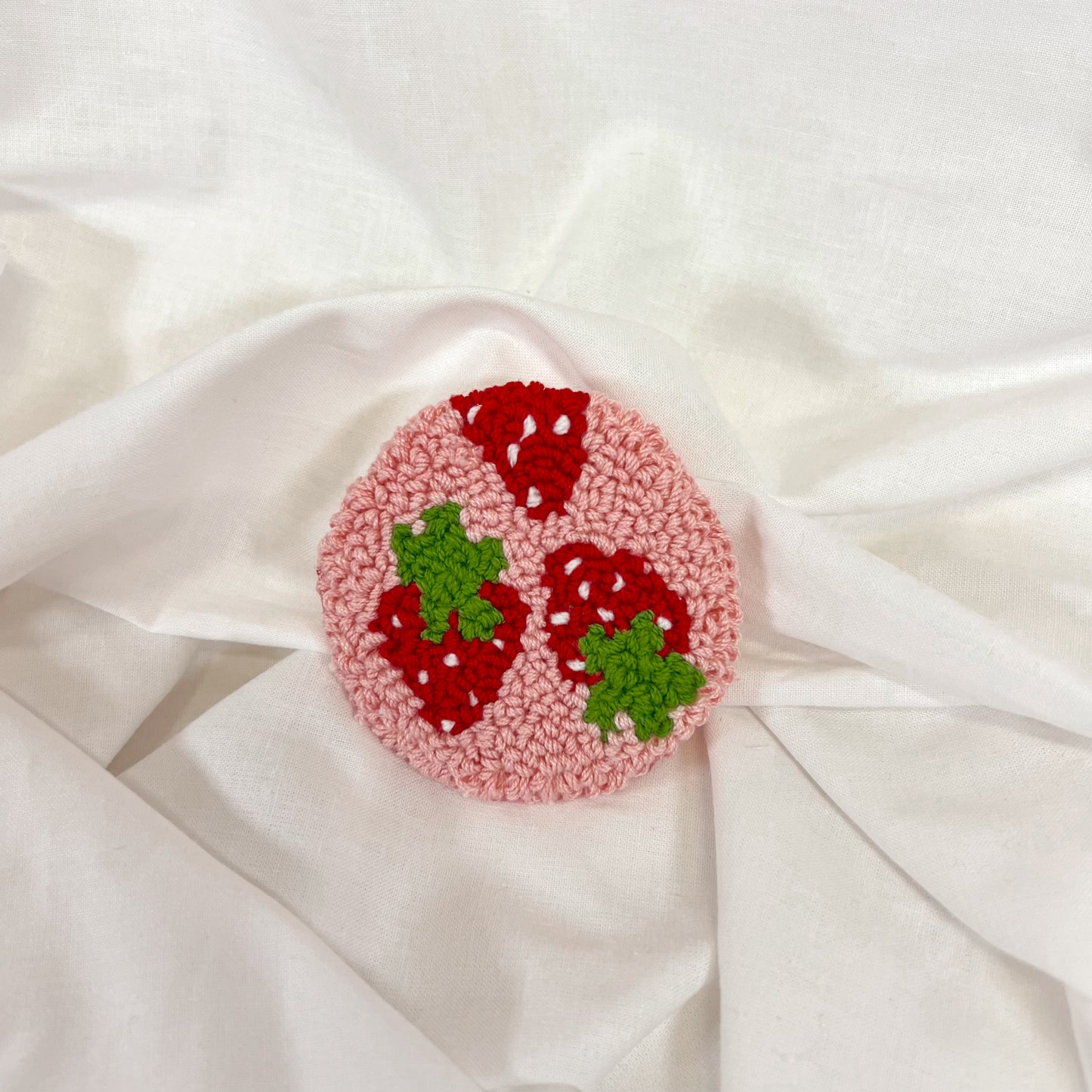 Circular pink tufted car coaster with red strawberries and green leaves on a white fabric background
