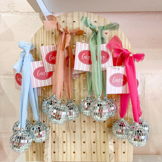 A series of ribbon disco ball car mirror hangings displayed on a wooden board, with ribbons in various colors and disco balls attached to each.