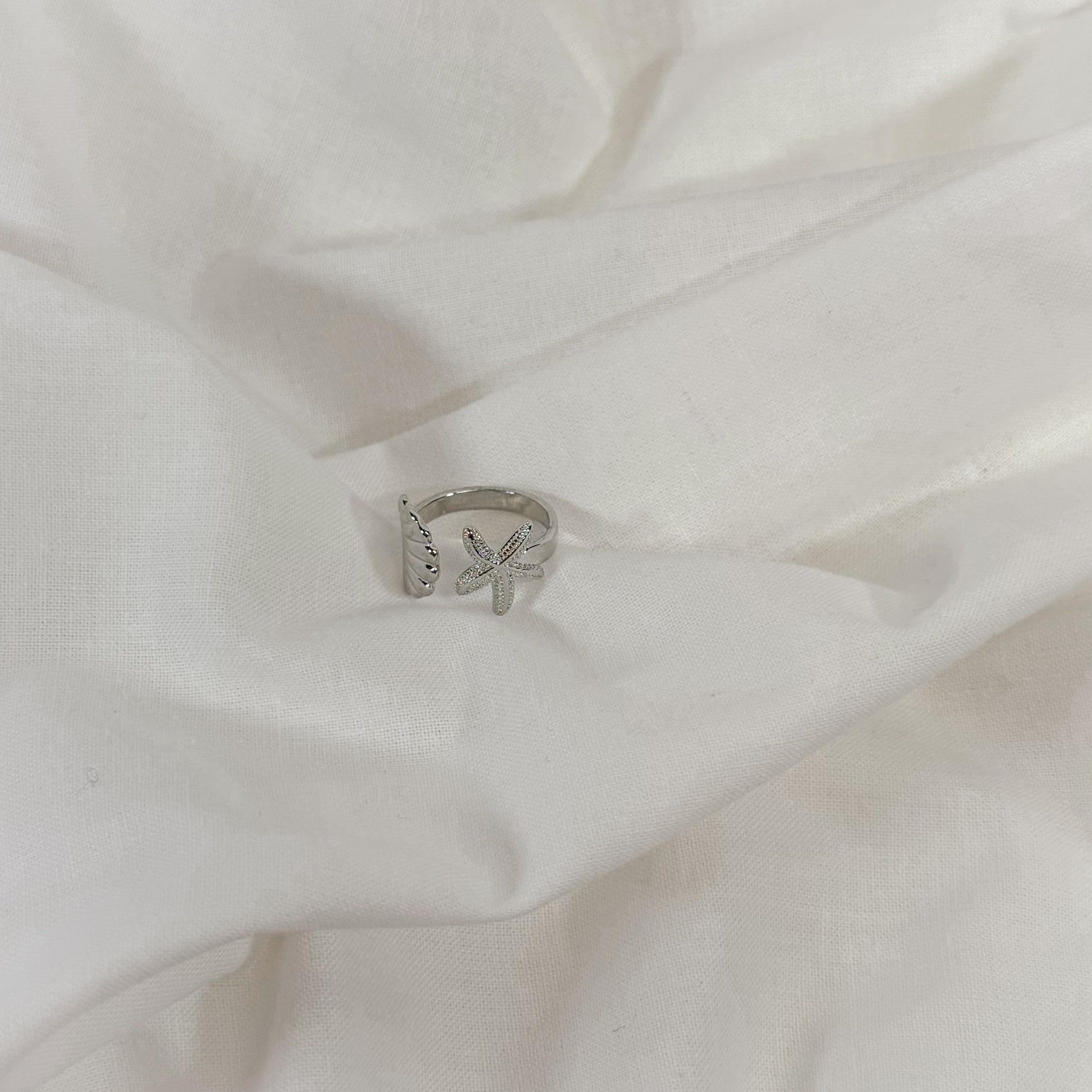 Silver ring with a shell design on a white fabric background