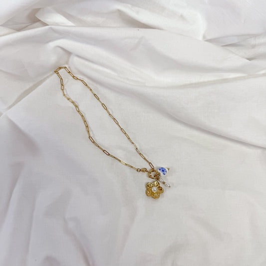 Gold necklace with a porcelain flower pendant on a white fabric background