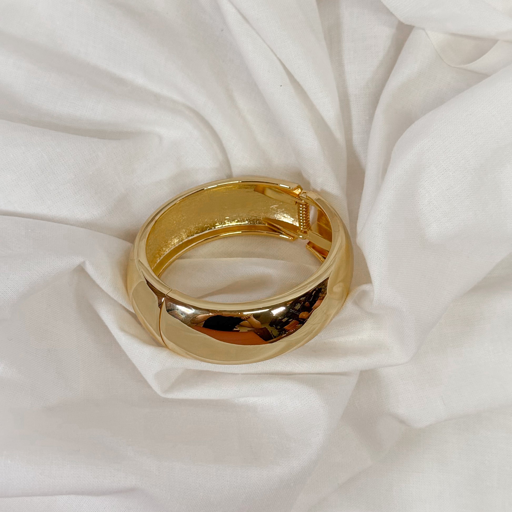 Gold colored chunky bracelet on a white fabric background