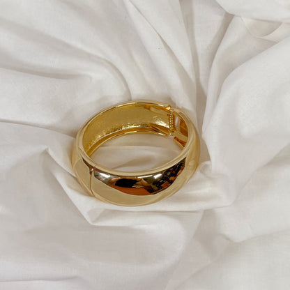 Gold colored chunky bracelet on a white fabric background