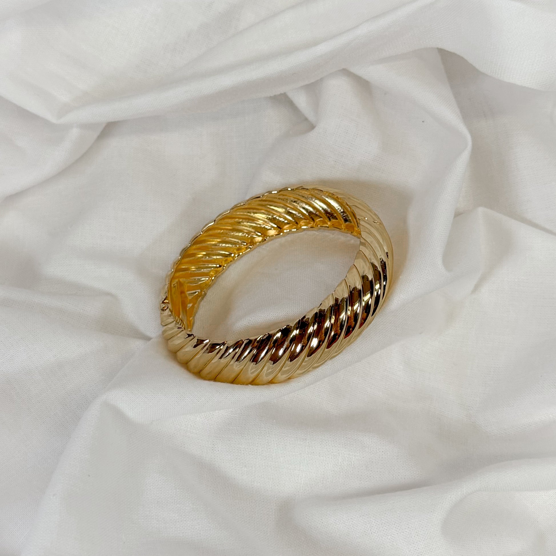 Patterned chunky gold bangle on a white fabric background