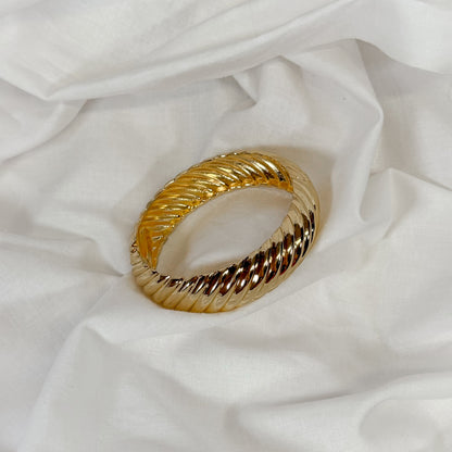 Patterned chunky gold bangle on a white fabric background