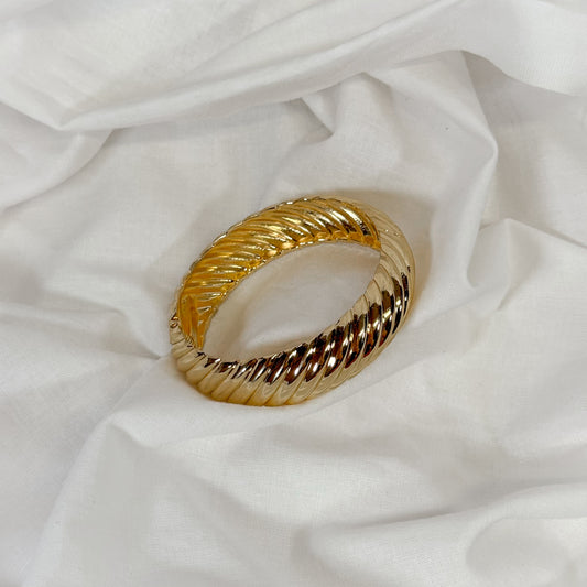 Patterned chunky gold bangle on a white fabric background