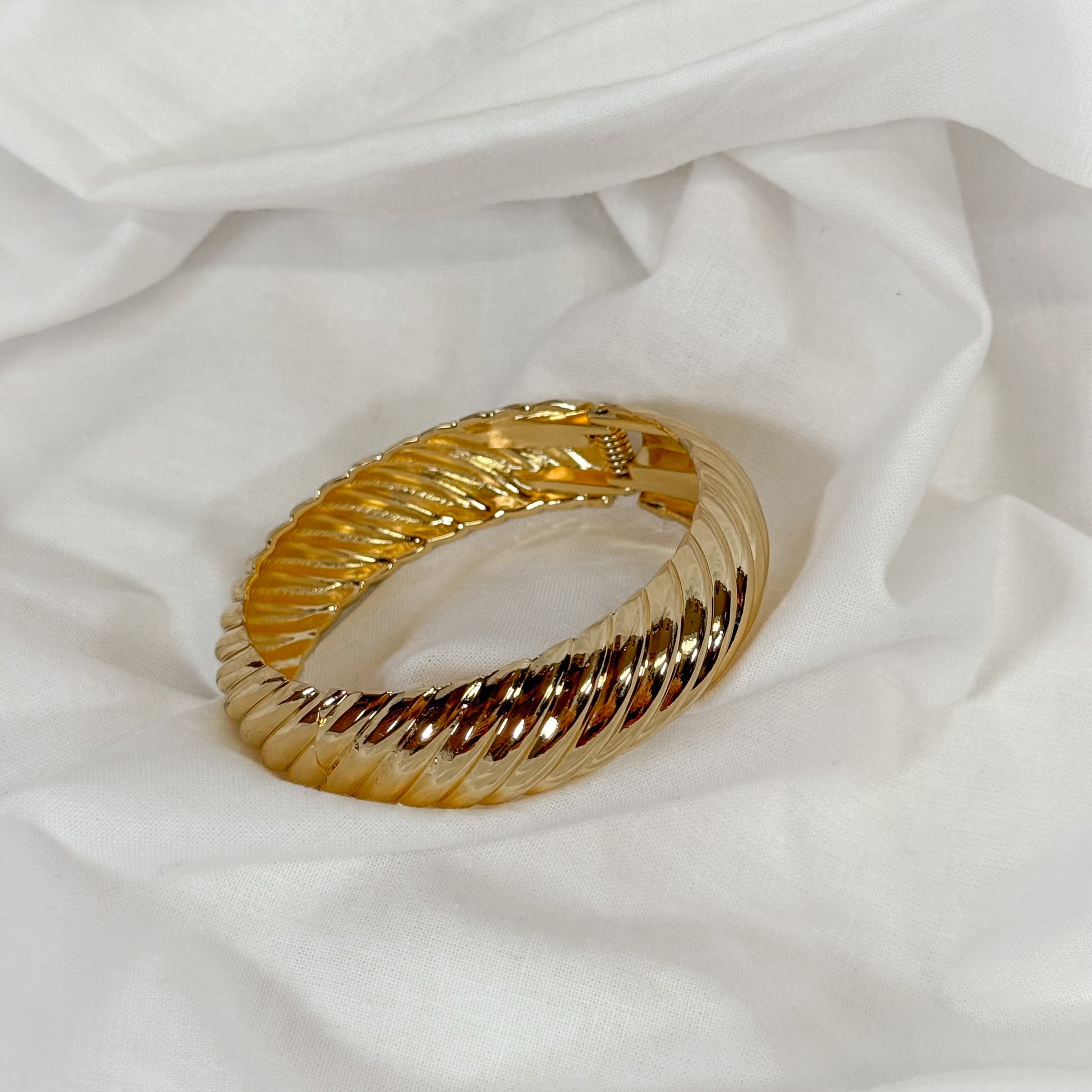 Gold bangle bracelet on a white fabric background