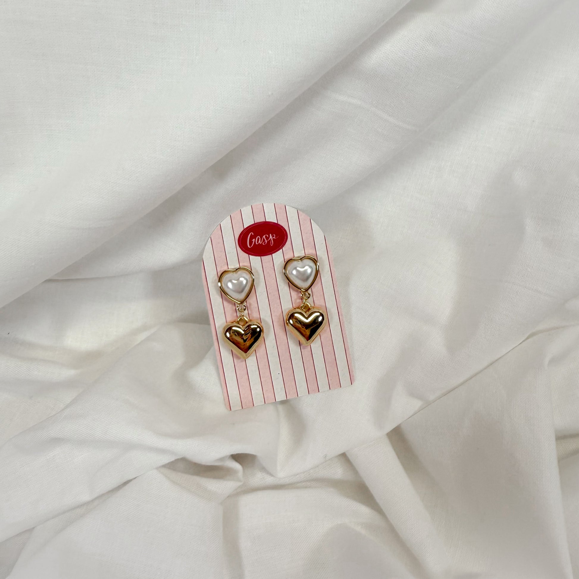 Pearl and gold heart shaped dangly earrings on a white fabric background
