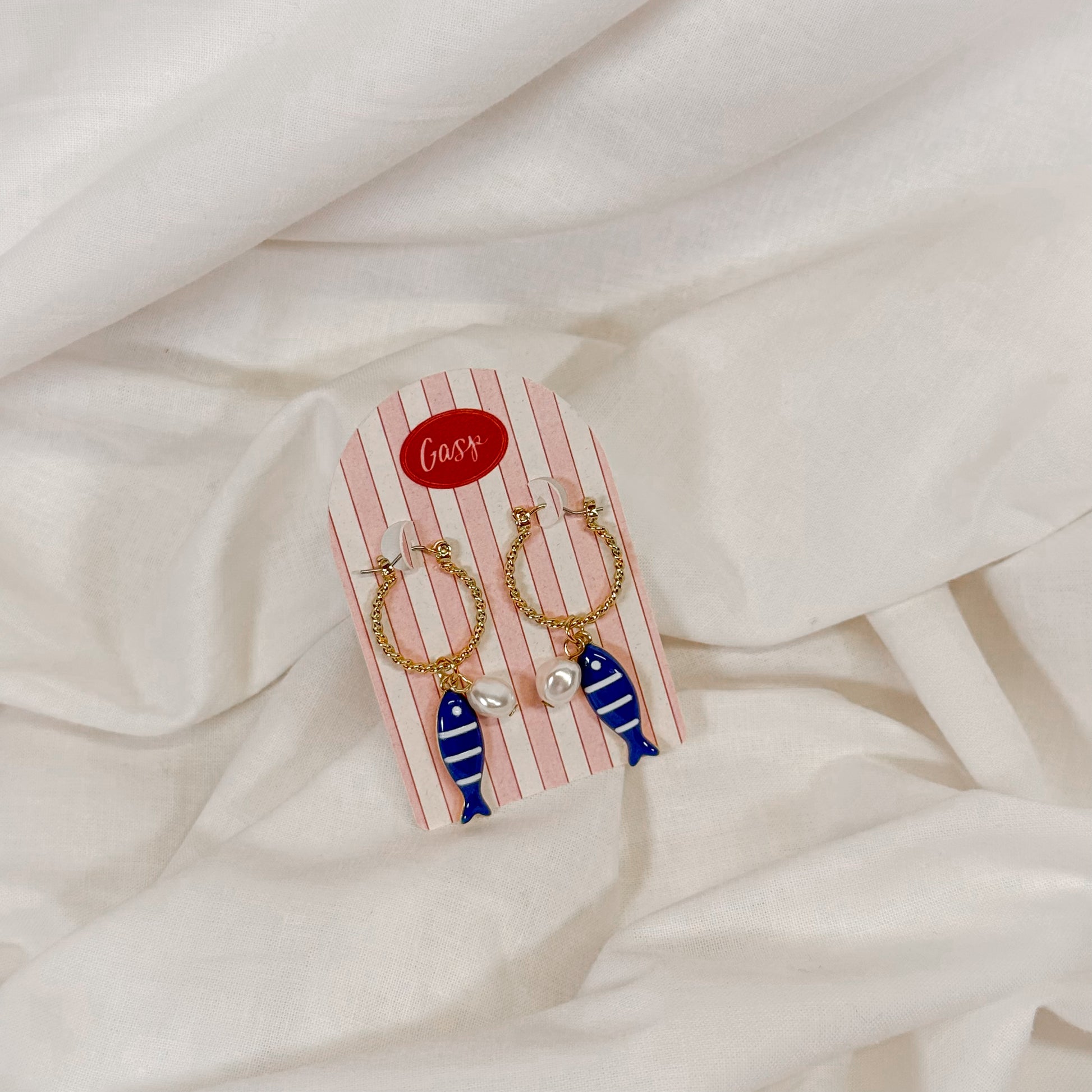 Pair of earrings with fish design on a striped card against a white fabric background