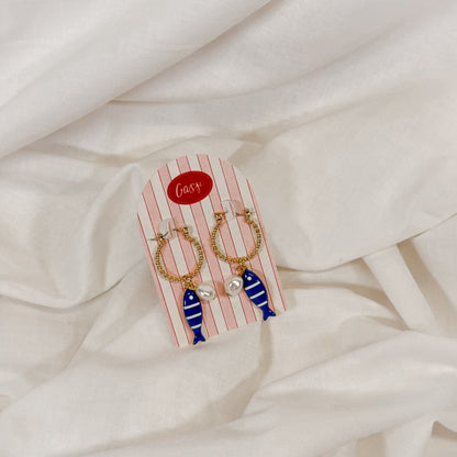 Pair of earrings with fish design on a striped card against a white fabric background
