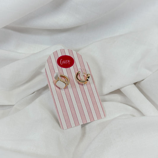 Gold huggie hoop earrings with square pearl charm on a white fabric background