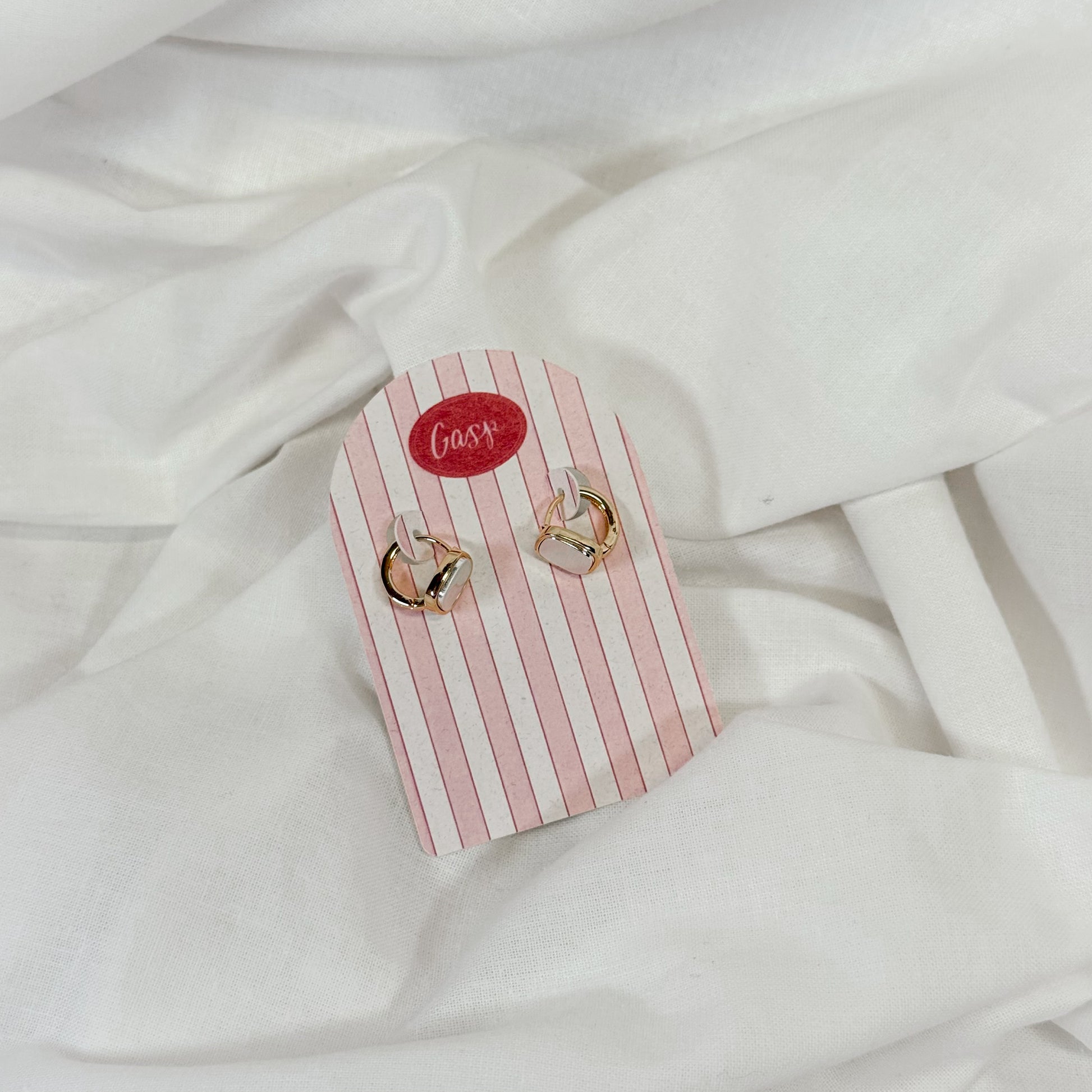 Pair of gold and pearl hoop earrings on a pink and white striped card with 'Gasp' branding, placed on a white fabric background.
