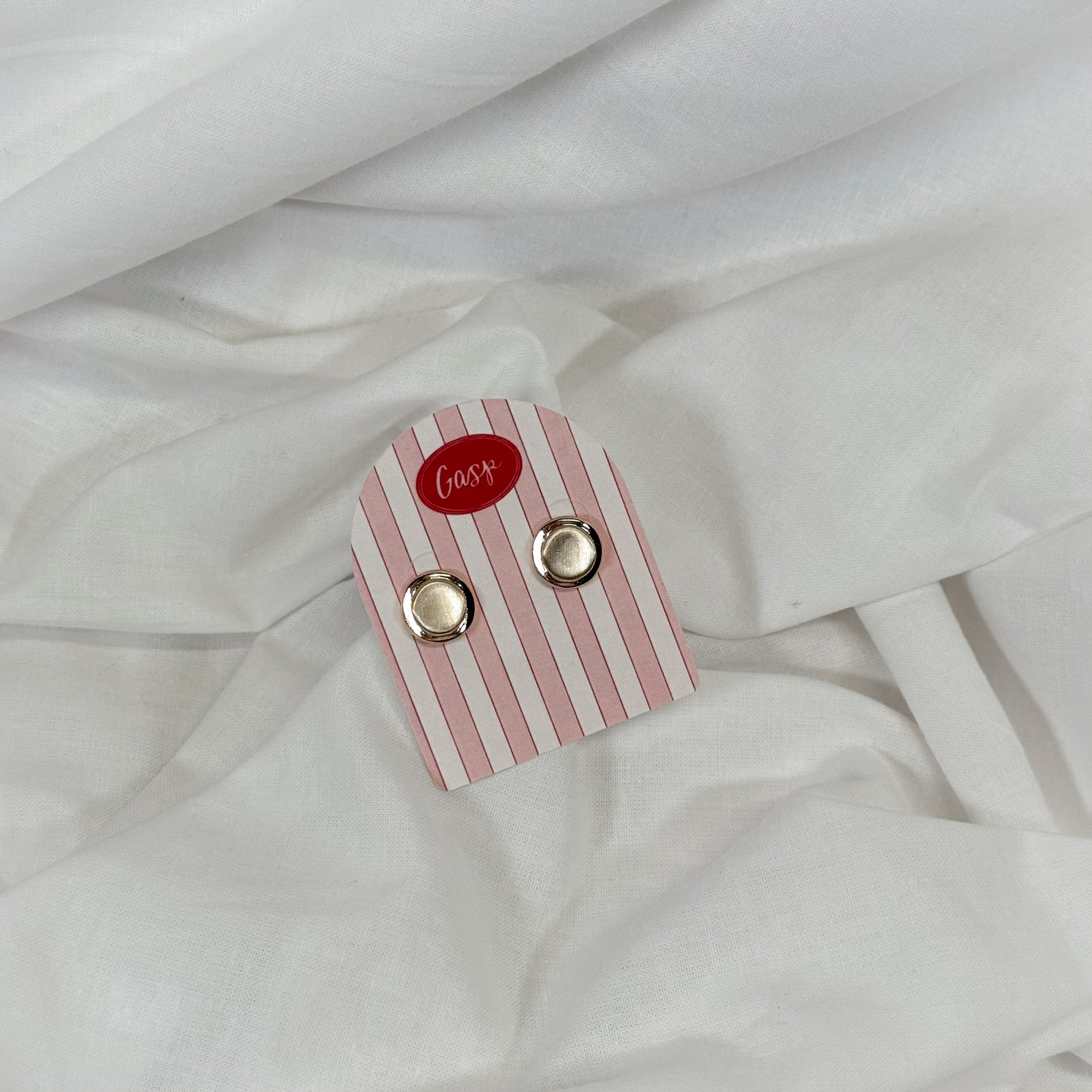 Flat gold earrings on a white fabric background