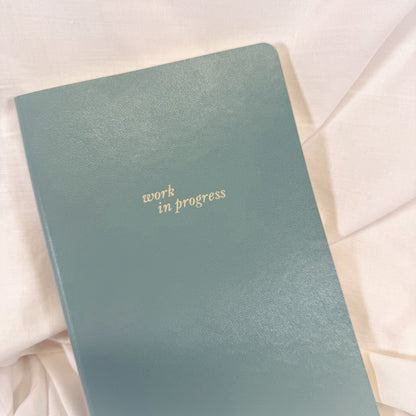 Blue notebook with 'work in progress' text on a light fabric background