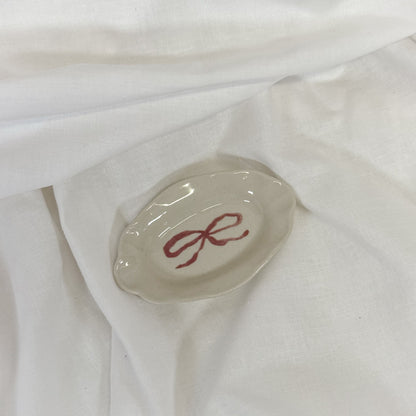 Small oval dish with a red bow design on a white fabric background