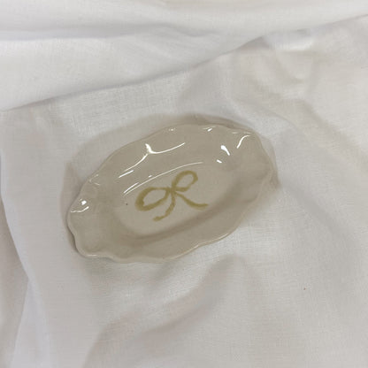 Small white dish with a yellow dainty bow on a white fabric background