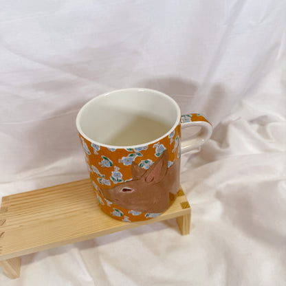 Orange mug with animal pattern on a wooden coaster against a white background